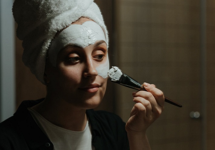 picture of a woman putting a clay hydrating face mask in front a mirror 