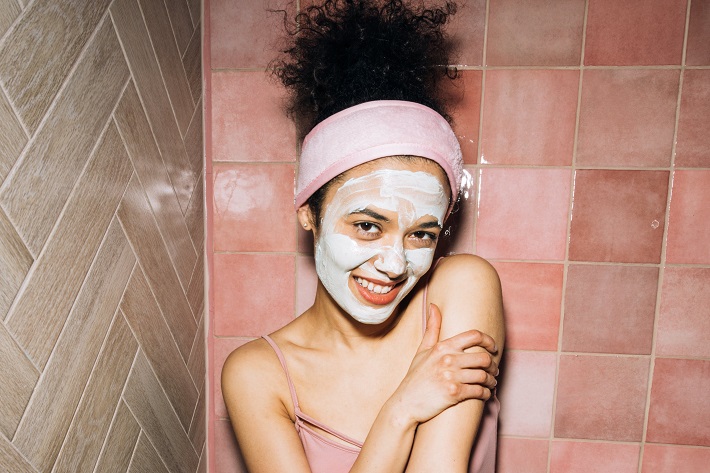 picture of a woman with a face hydrating mask in front a pink tile shower