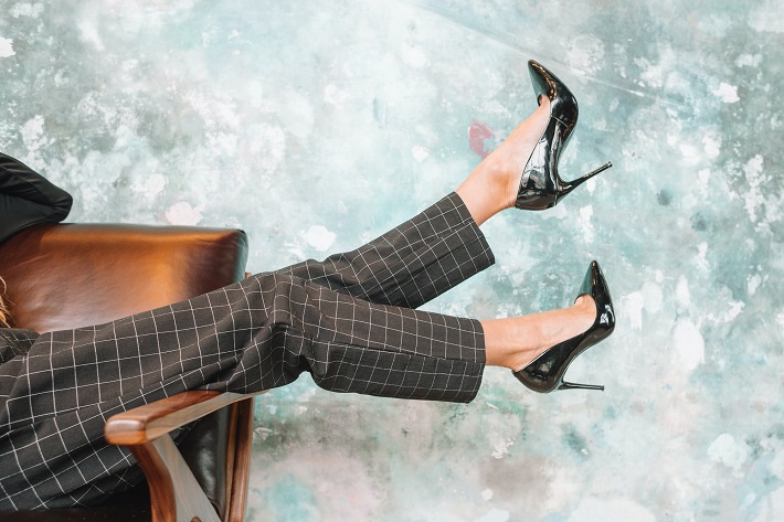 picture of a woman in comfortable high heels on a brown sofa in front a blue wall 