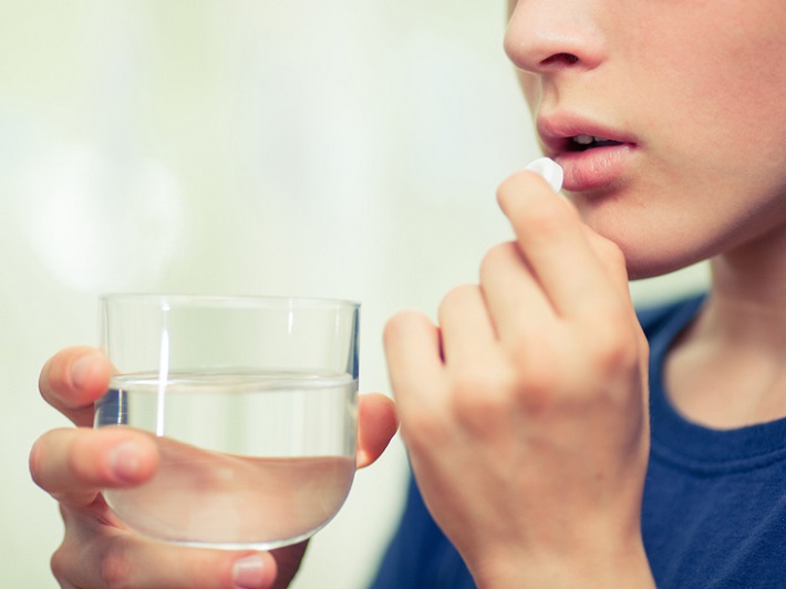 picture of a woman drinking water and taking a pill
