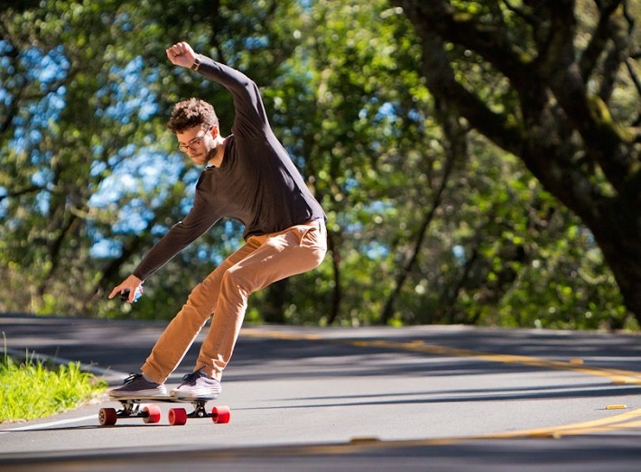 man turning with electric skateboard with orange wheels down a road 