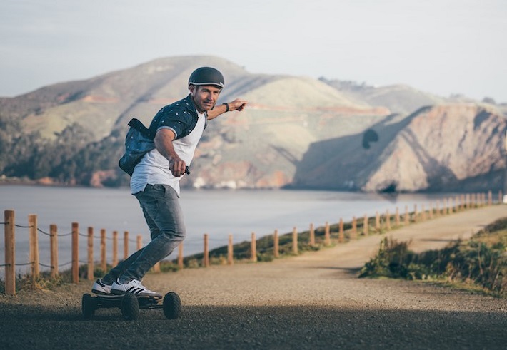 man riding an electric skateboard on a gravel road 