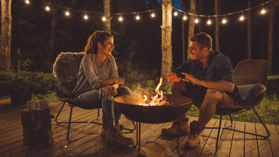 a man and a woman sit outside by a fire pit
