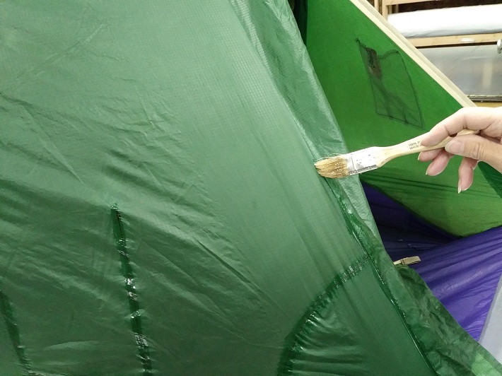 Repairing a green tent with seam grip.