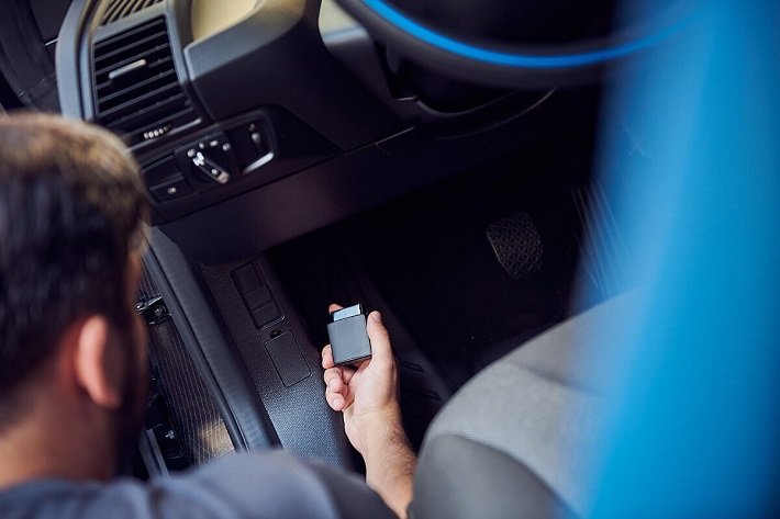 Man holding GPS tracker while kneeling by the car