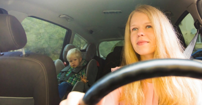 a mother driving the car with her kid in the backseat sitting in a car seat booster