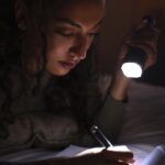 woman using a flashlight to read in the dark